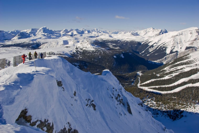 Skiers walk along the edge of Delirium Dive, Sunshine Village Ski Resort, Banff National Park, Alberta, Canada.